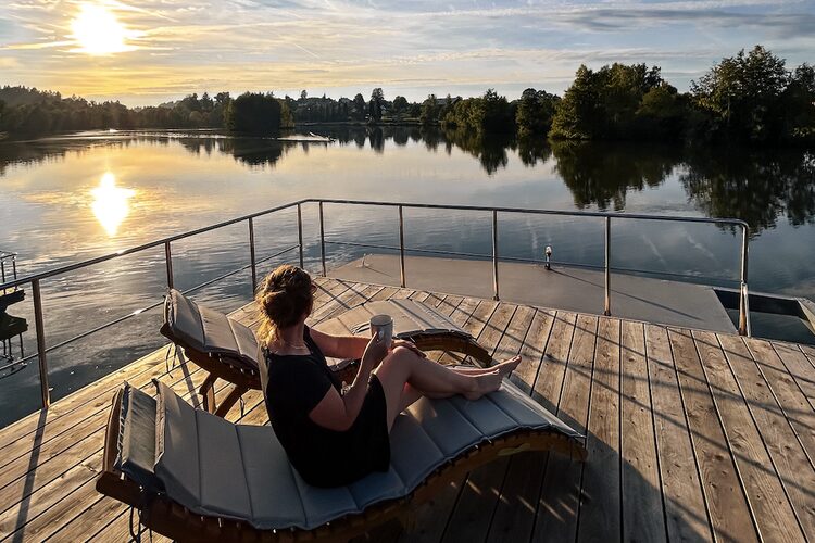 Eine Frau genie&szlig;t ein Getr&auml;nk auf einer Liege auf dem Sonnendeck eines Hausboots.