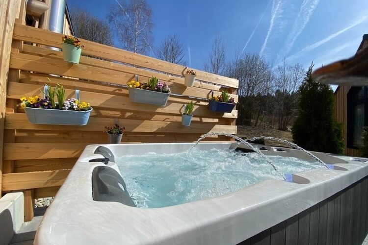 Ein Whirlpool steht vor einer Holzwand auf einer Chalet-Terrasse.