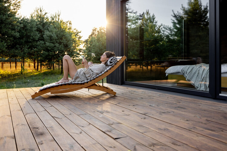 Eine Frau liegt auf einer Liege auf der Holzterrasse.