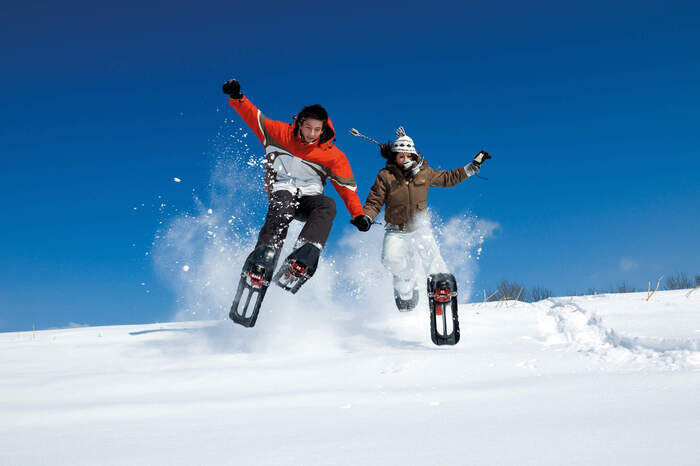 Zwei Personen springen in Schneeschuhen einen H&uuml;gel hinunter.