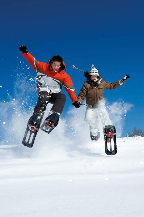Zwei Personen springen in Schneeschuhen einen Hügel hinunter.
