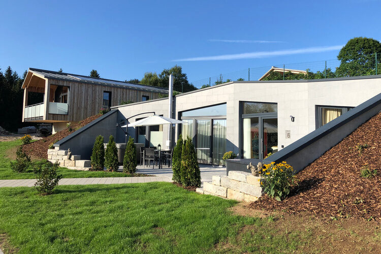 Ein in den Boden eingelassenes Chalet mit einer großen Terrasse und vielen Fenstern.