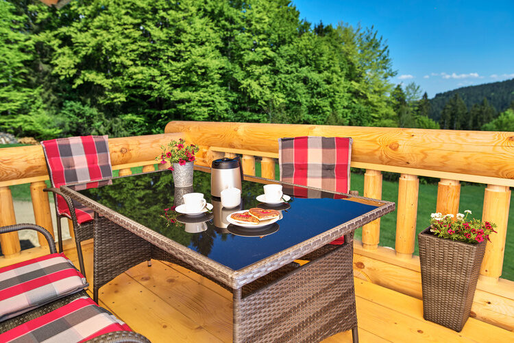 Ein Tisch und Stühle auf der Terrasse des Chalet Blumental vor einem baumbestandenen Hintergrund.