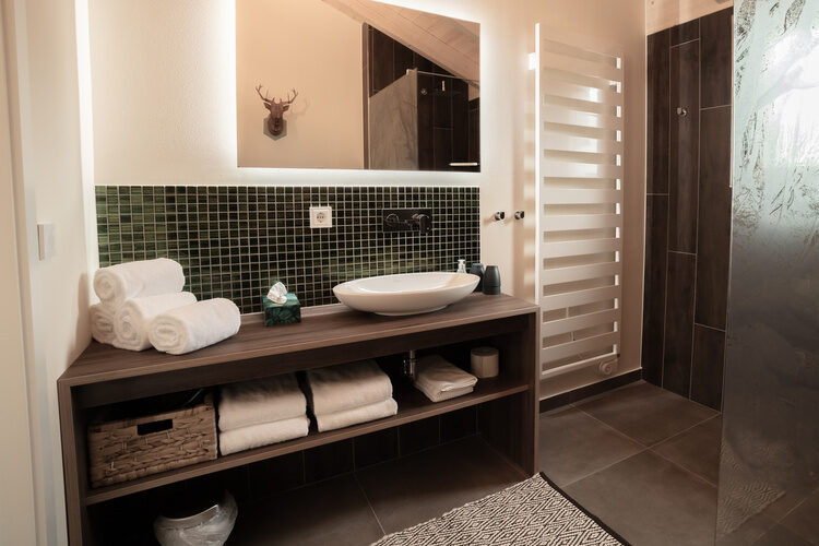 Das modern eingerichtete Badezimmer im Chalet mit einer schwarzen Armatur und eine großen Spiegel
