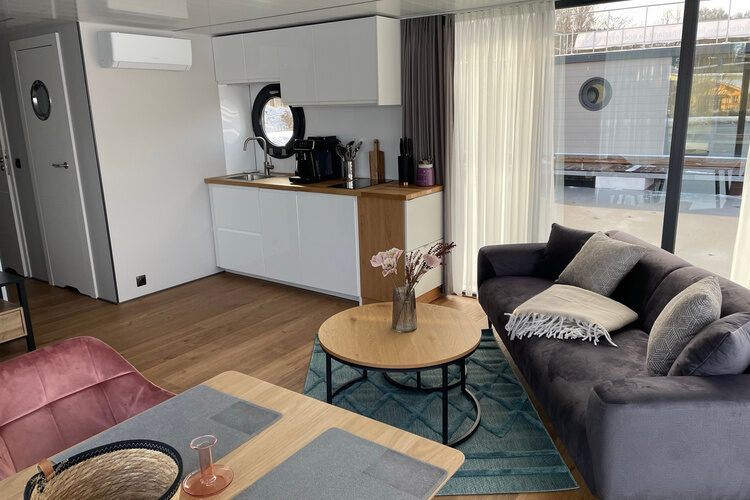 Ein gem&uuml;tliches Wohnzimmer mit Sofa und gro&szlig;er Fensterfront im Chaletdorf Im Waidlerland.